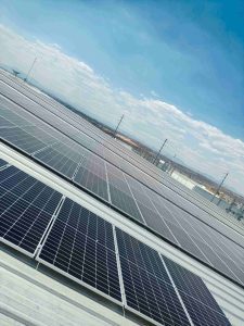 one thousand solar panels install over a white rooftop, blue sky with a few clouds in the background